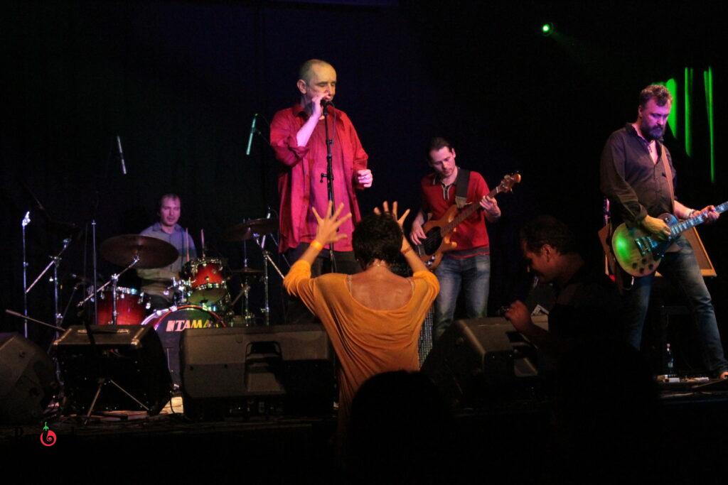The Hungarian underground band Európa Kiadó on stage at B32 cultural center in Budapest, with the singer in a red shirt and audience members dancing close to the stage.